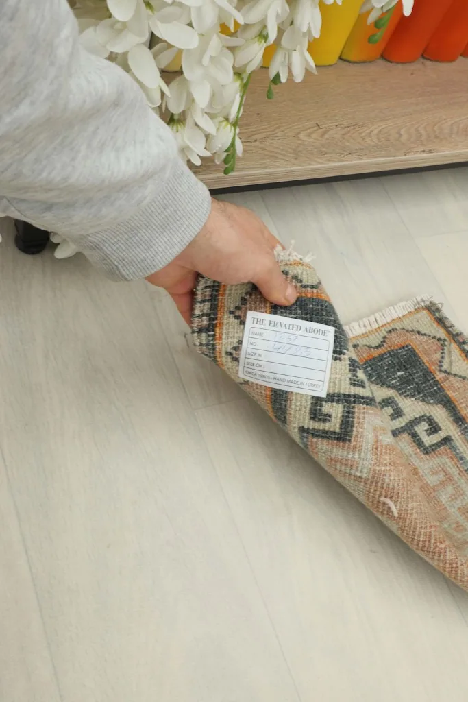 Hand holding the folded rug, revealing the back of the rug and a care label