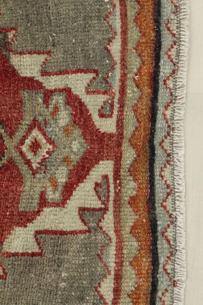 Close-up detail of the rug's border and corner, showing the rust, orange, and gray geometric patterns.