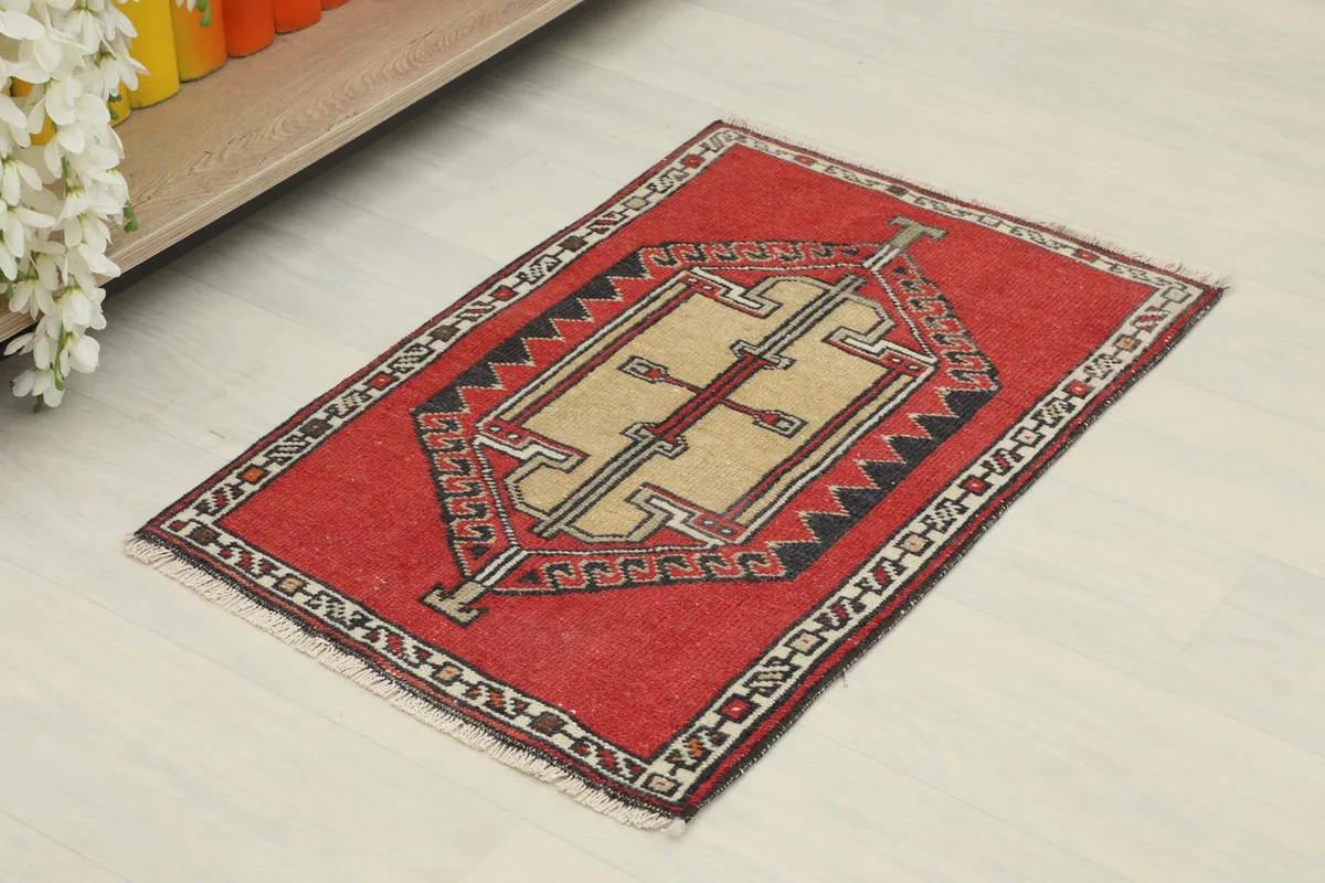 Angled view of the hand-knotted doormat, showing its red field and central beige motif.