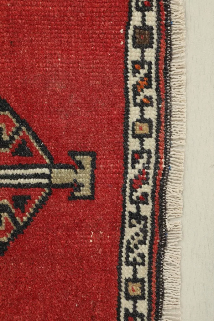 Close-up detail of the doormat's red pile and intricate ivory and black border design.