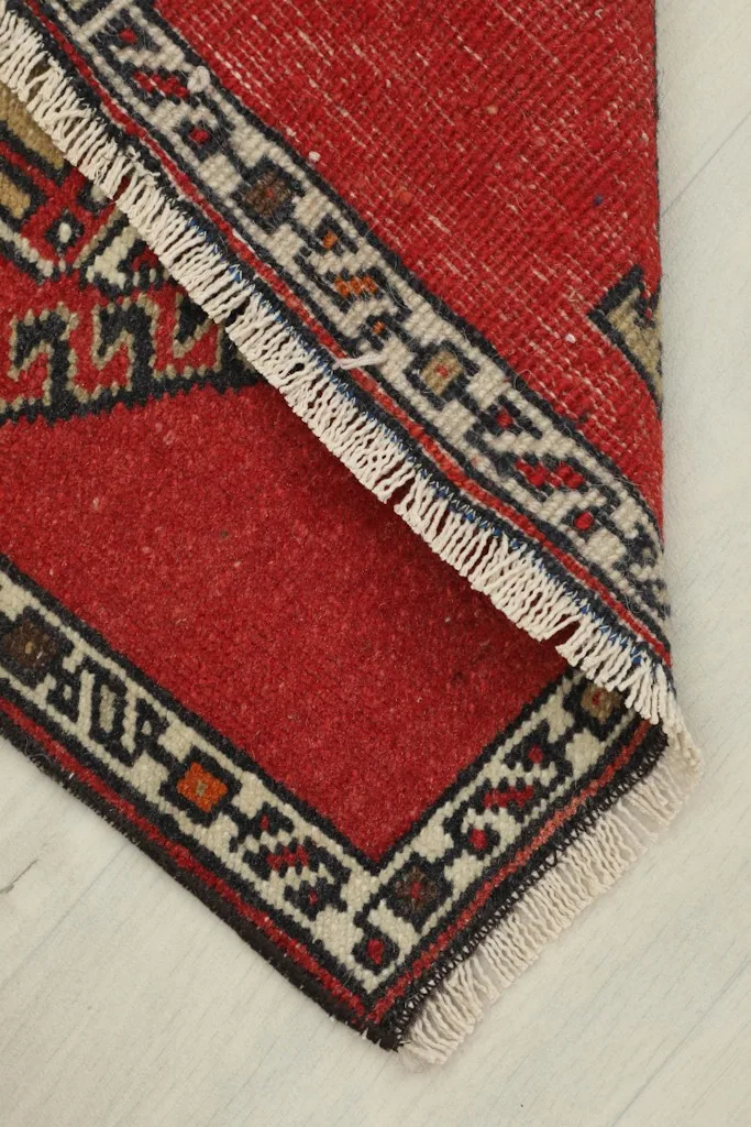 View of the doormat folded, revealing the texture of the red wool pile and cotton foundation.