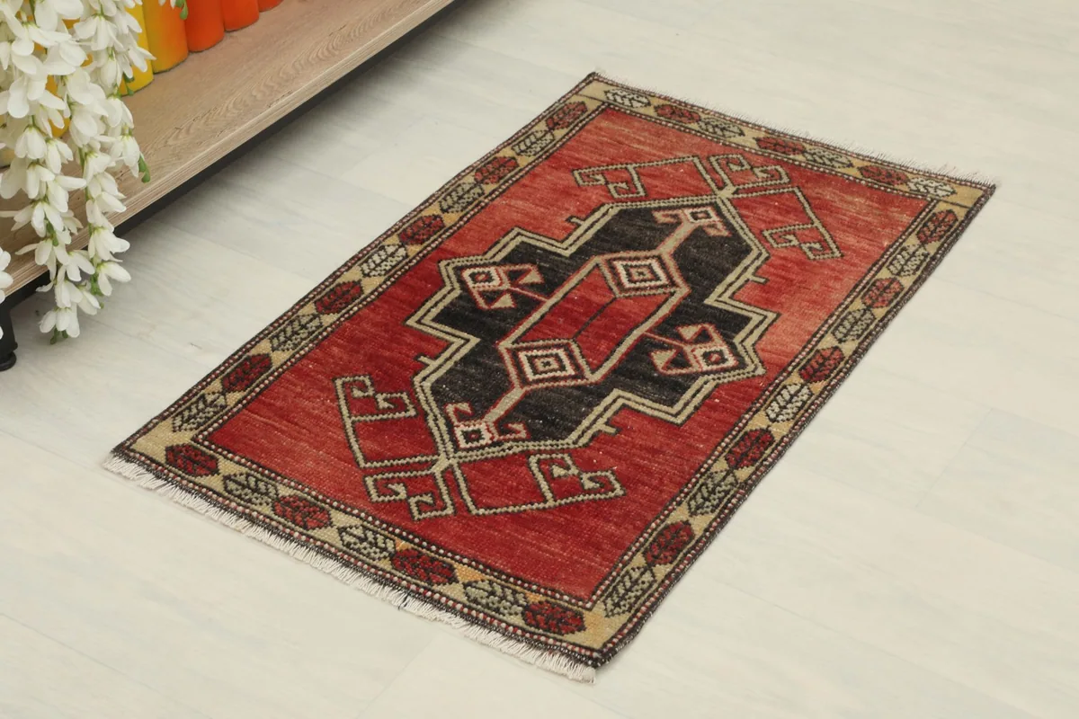 Angled view of the vintage red rug, showcasing its black central motif and tan border details.