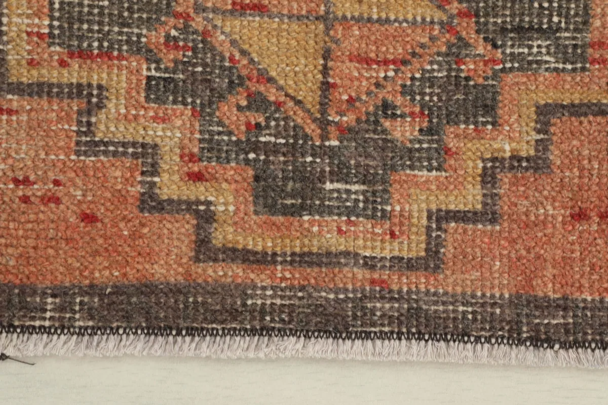 Close-up detail of the rug's geometric pattern in orange, gold, and charcoal, showing texture.