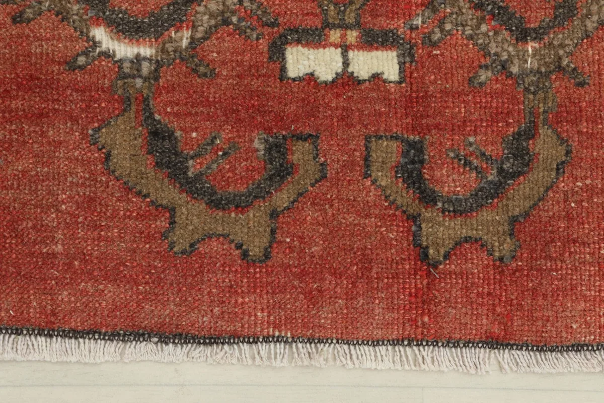 Close-up detail of the bottom edge of the rust doormat, showing tribal motifs and fringe.