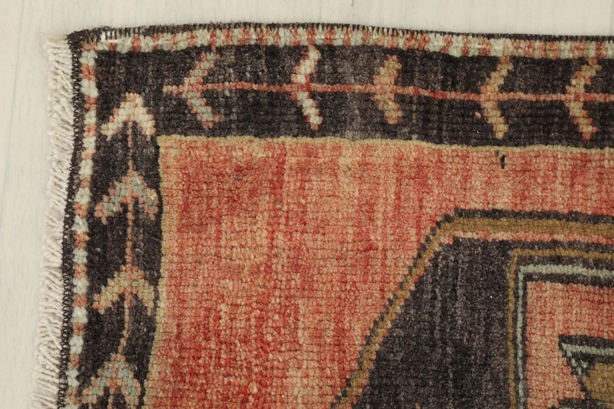 Corner detail showing the charcoal border design and the faded rust field of the vintage rug.