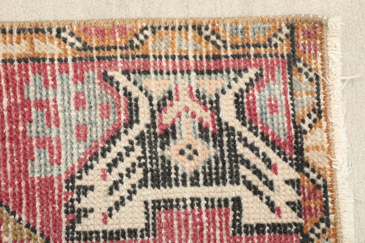 Close-up of a tribal motif near the corner, featuring black and beige elements on a rose background