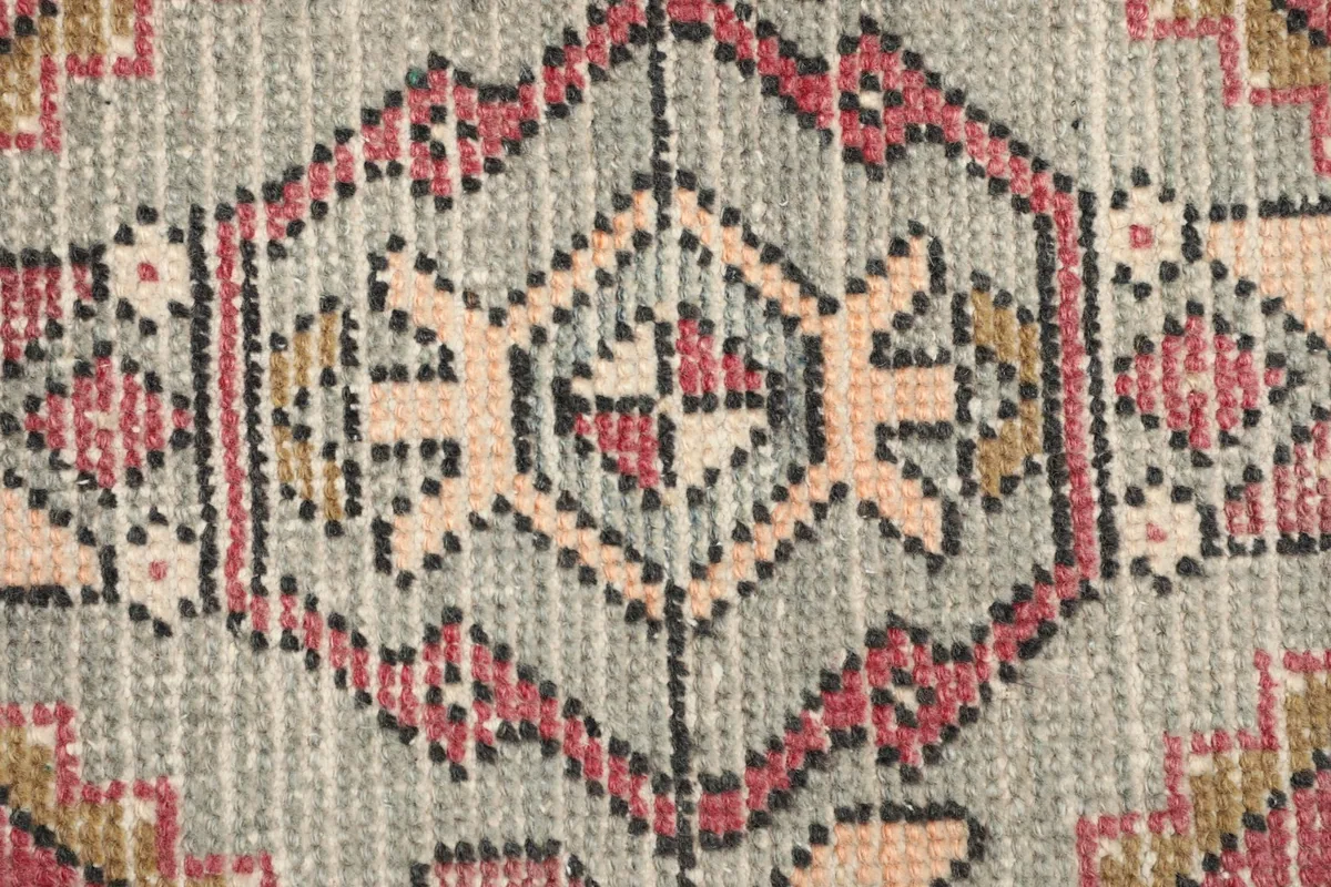 Detailed view of the low wool pile texture and knotting in the gray and rose colors