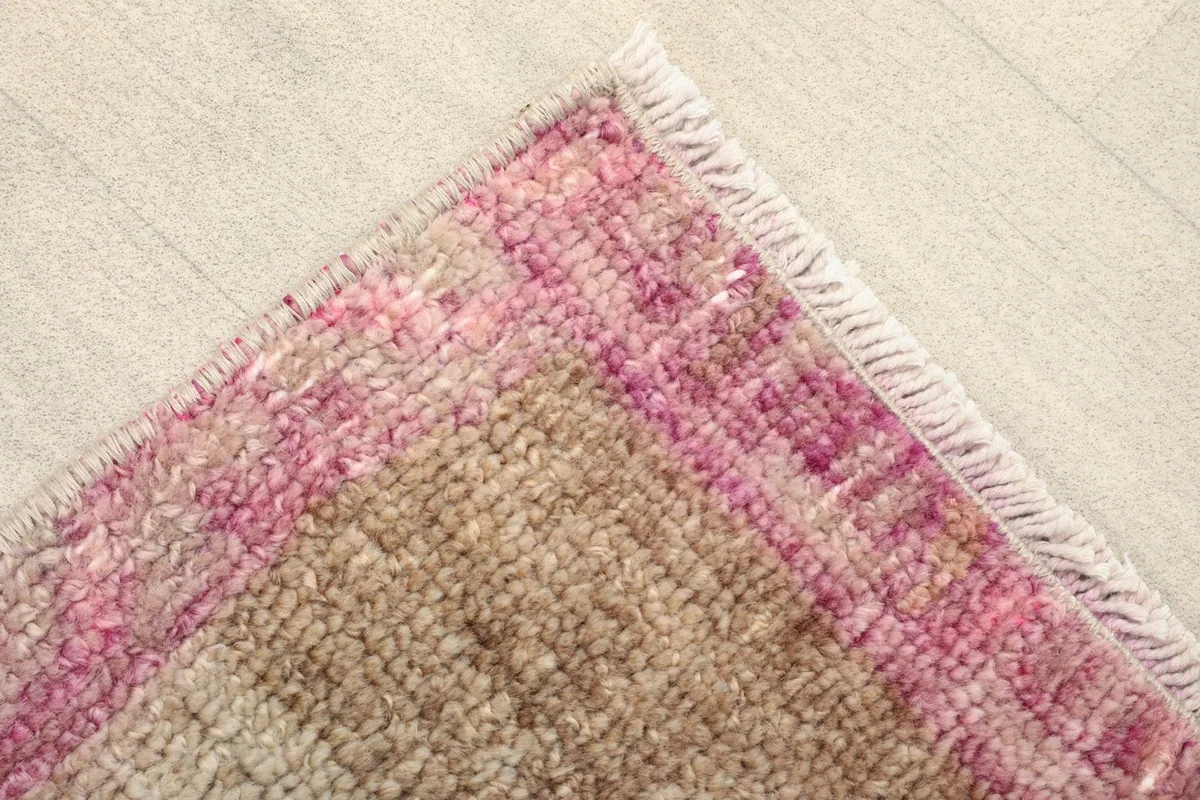 Close-up detail of the rug's corner, highlighting the pink border and wool texture
