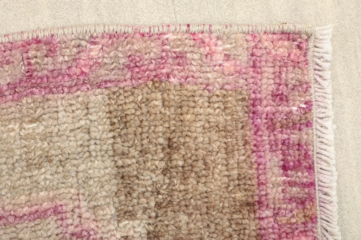 Detailed view of the rug's pink patterned border and part of the beige field