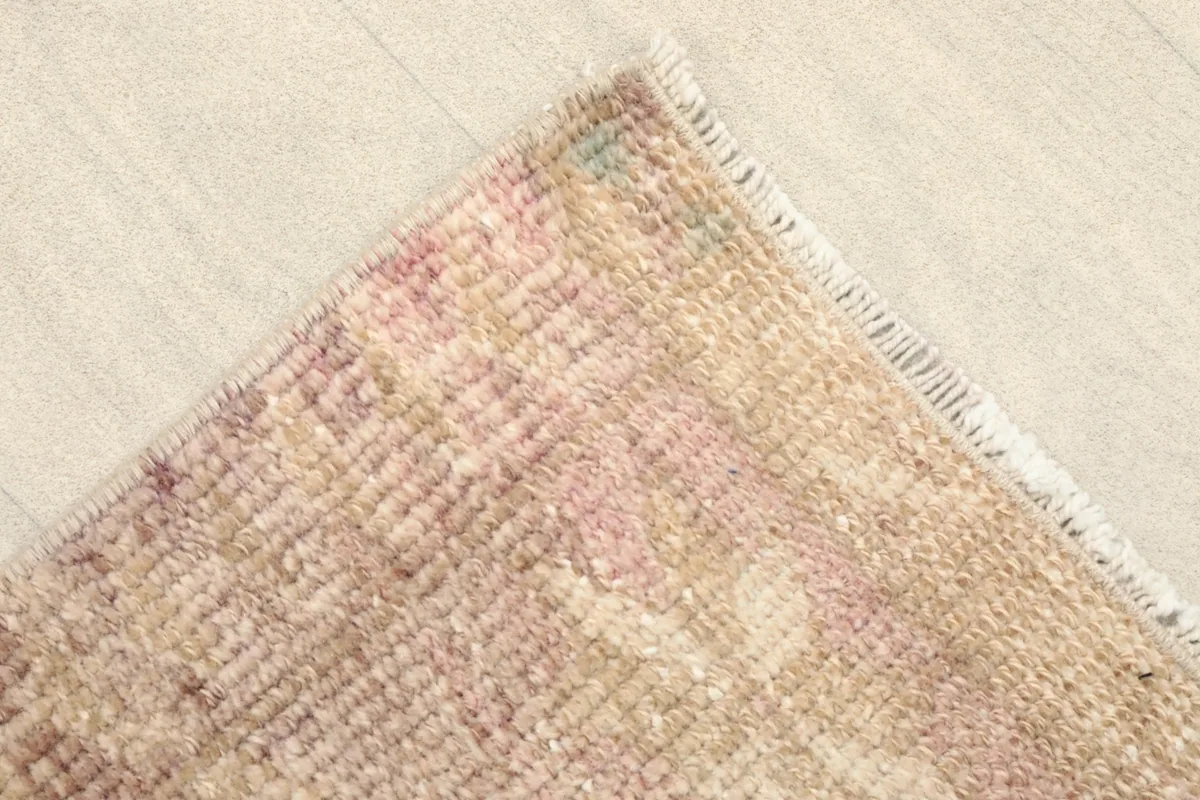 Corner detail of the rug, revealing the soft pink and beige tones and the short fringe.