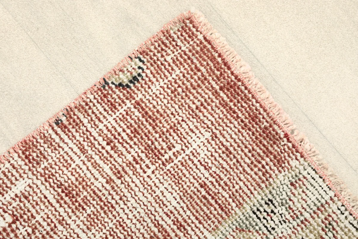 Detail of the rug's edge, showing the rust field and subtle border elements