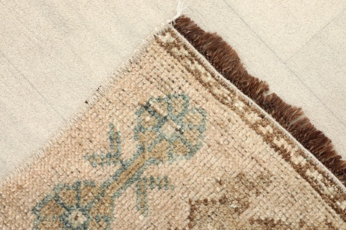 Close-up detail of the doormat's corner, showing the hand-knotted wool pile in tan and olive tones.