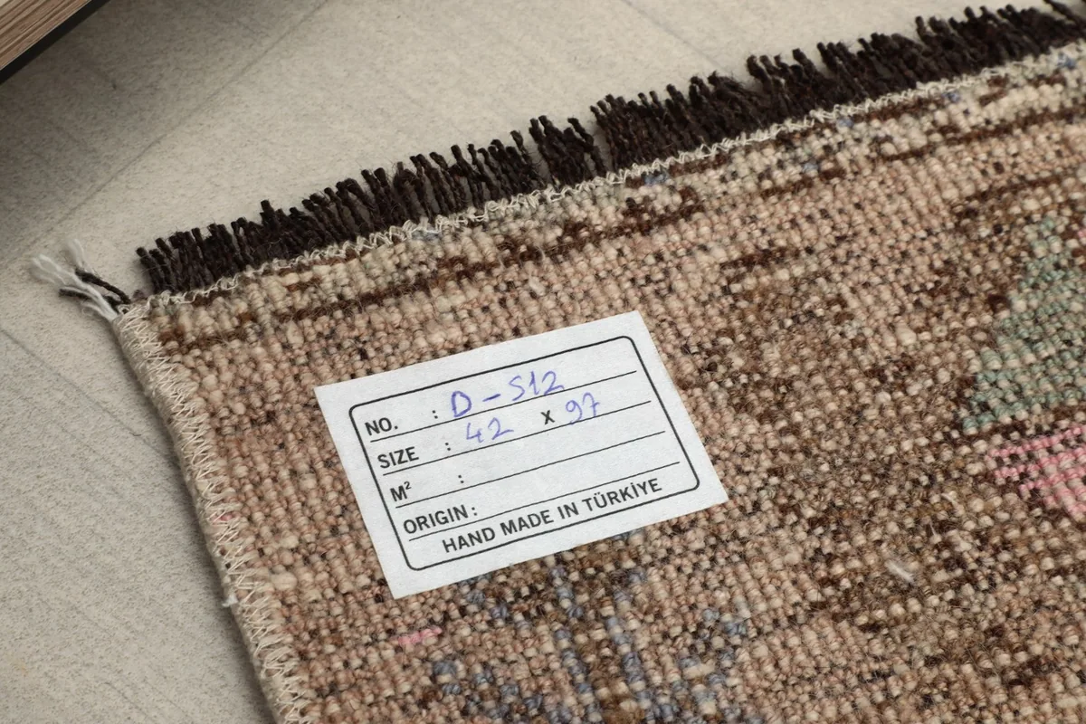 Back view of the doormat, showing the cotton foundation and a label with size and origin details.