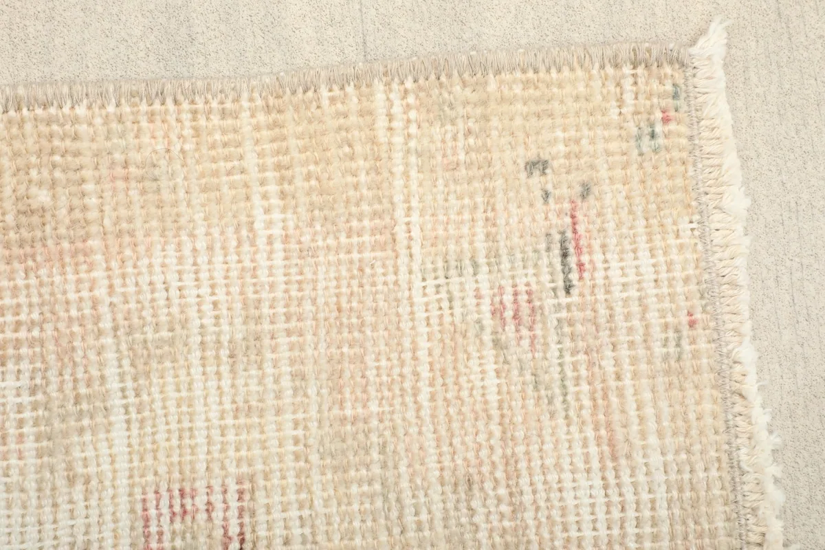 Close-up detail of the faded geometric patterns in rose and green on the beige field of the rug