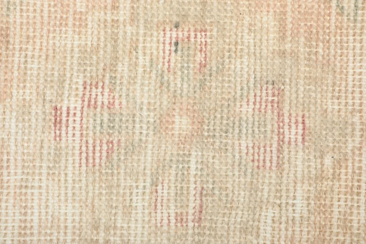 Close-up of a central geometric motif with faded rose and green threads on the beige background