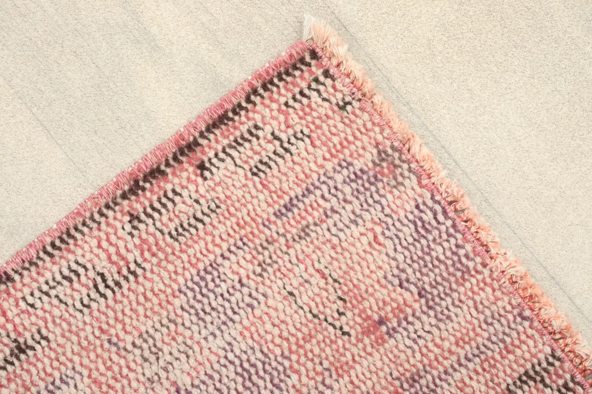 Corner detail of the rose rug, highlighting the worn pile and short fringe.