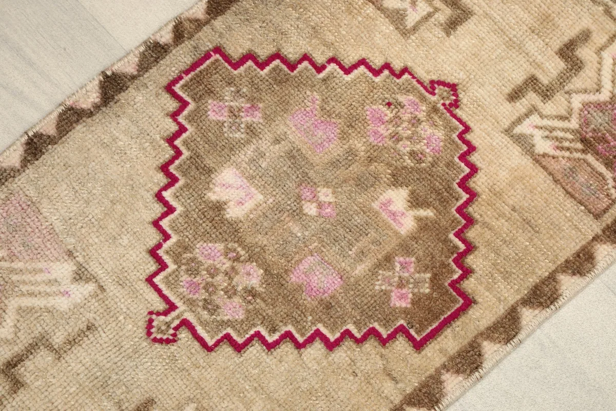Close-up detail of the rug's central geometric medallion with pink and brown accents on a beige field.