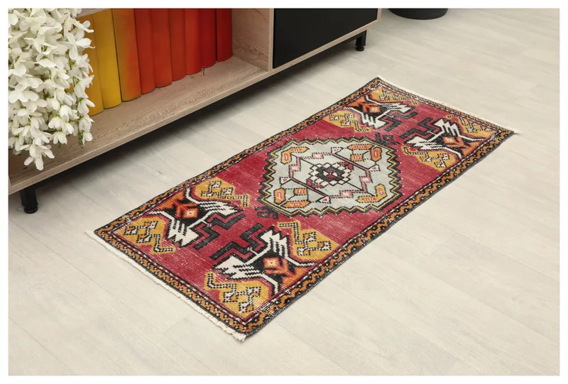 Full top view of the red and gray tribal medallion doormat on a light floor, next to a shelf.