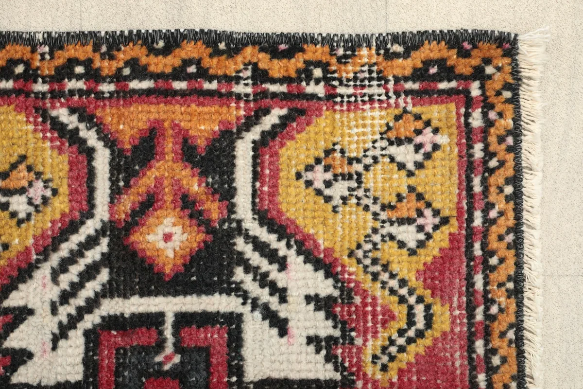 Close-up of the red field and the yellow, black, and ivory tribal patterns on the rug.