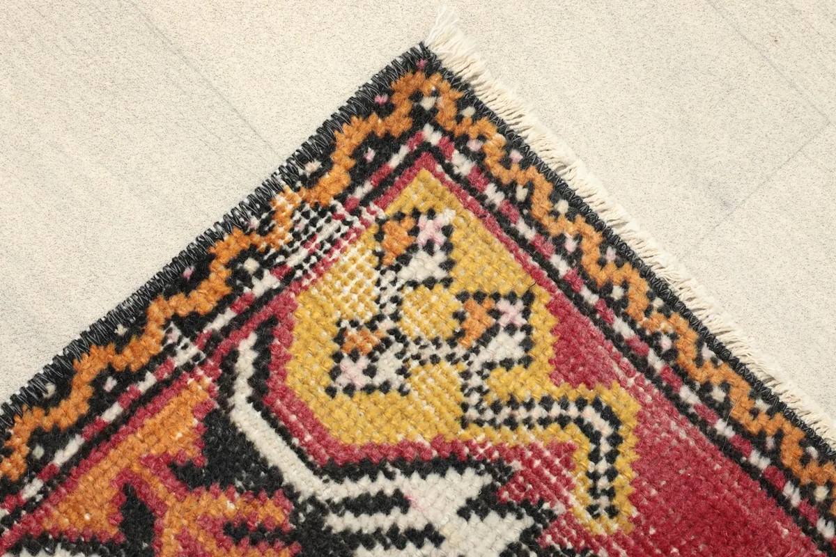 Corner view showing the red field, yellow and black tribal motifs, and the rug's border.