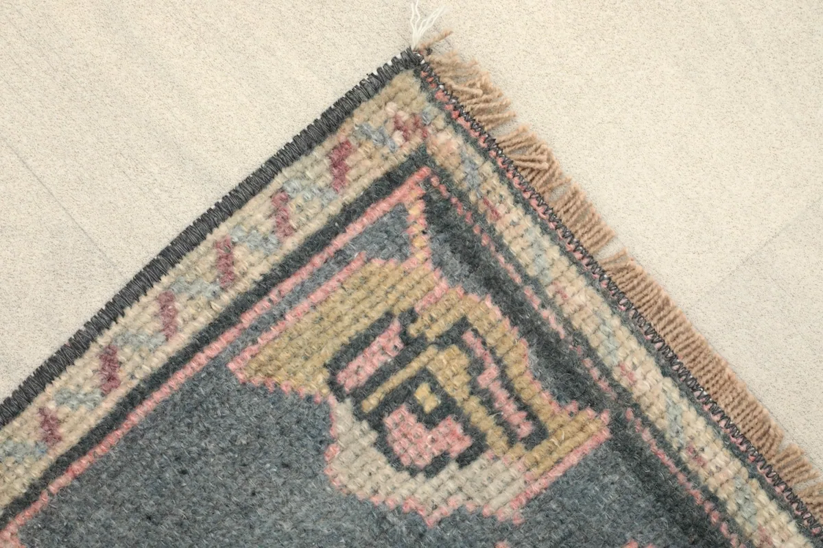 Corner view highlighting the gray border with small rose and beige details, and natural fringe.