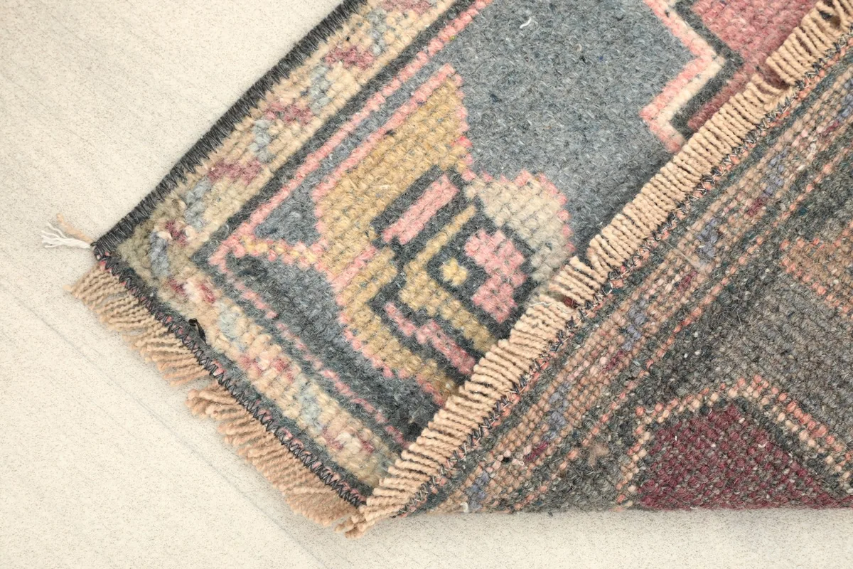 Folded corner of the rug, revealing the texture of the low wool pile and cotton foundation.