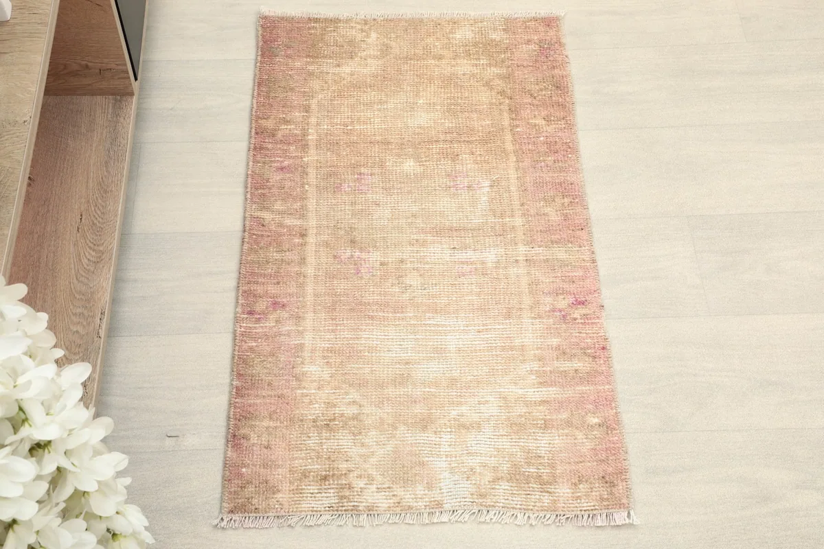 Overhead view of the small hand-knotted rug, showcasing its faded pink and beige colors and subtle design.
