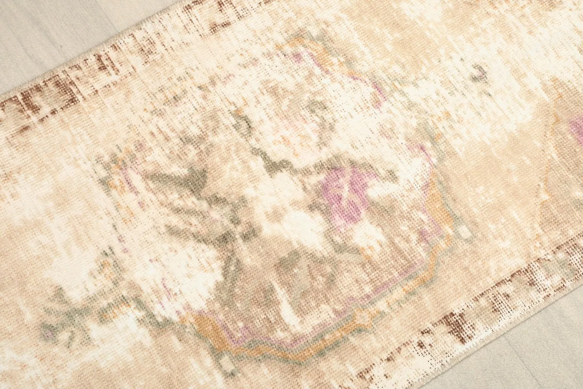 Close-up detail of the rug's surface, highlighting the faded pink, purple, and green patterns.