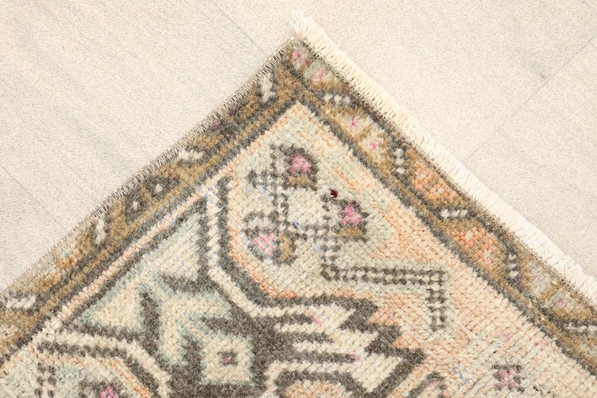 Detail of a corner, showing the brown border and geometric patterns in charcoal and rose.