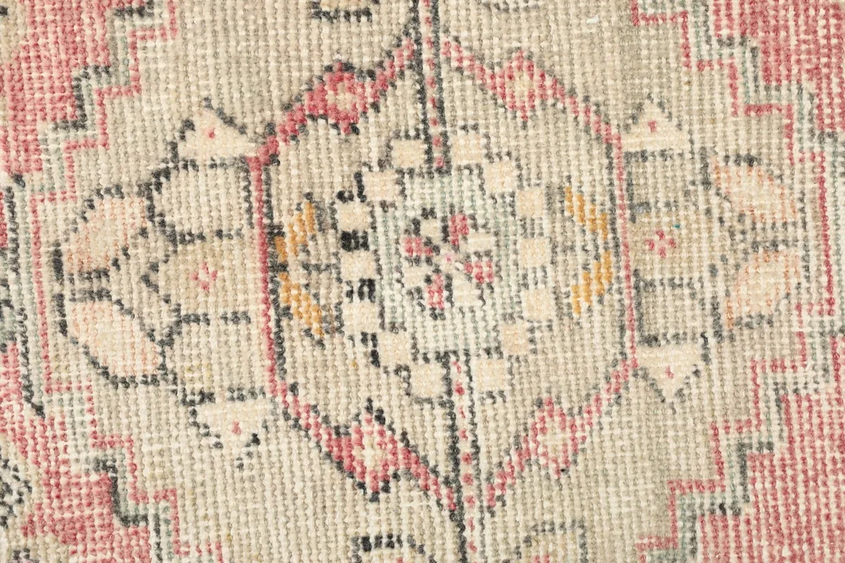 Close-up detail of the central medallion and surrounding geometric motifs in beige, rose, and black.