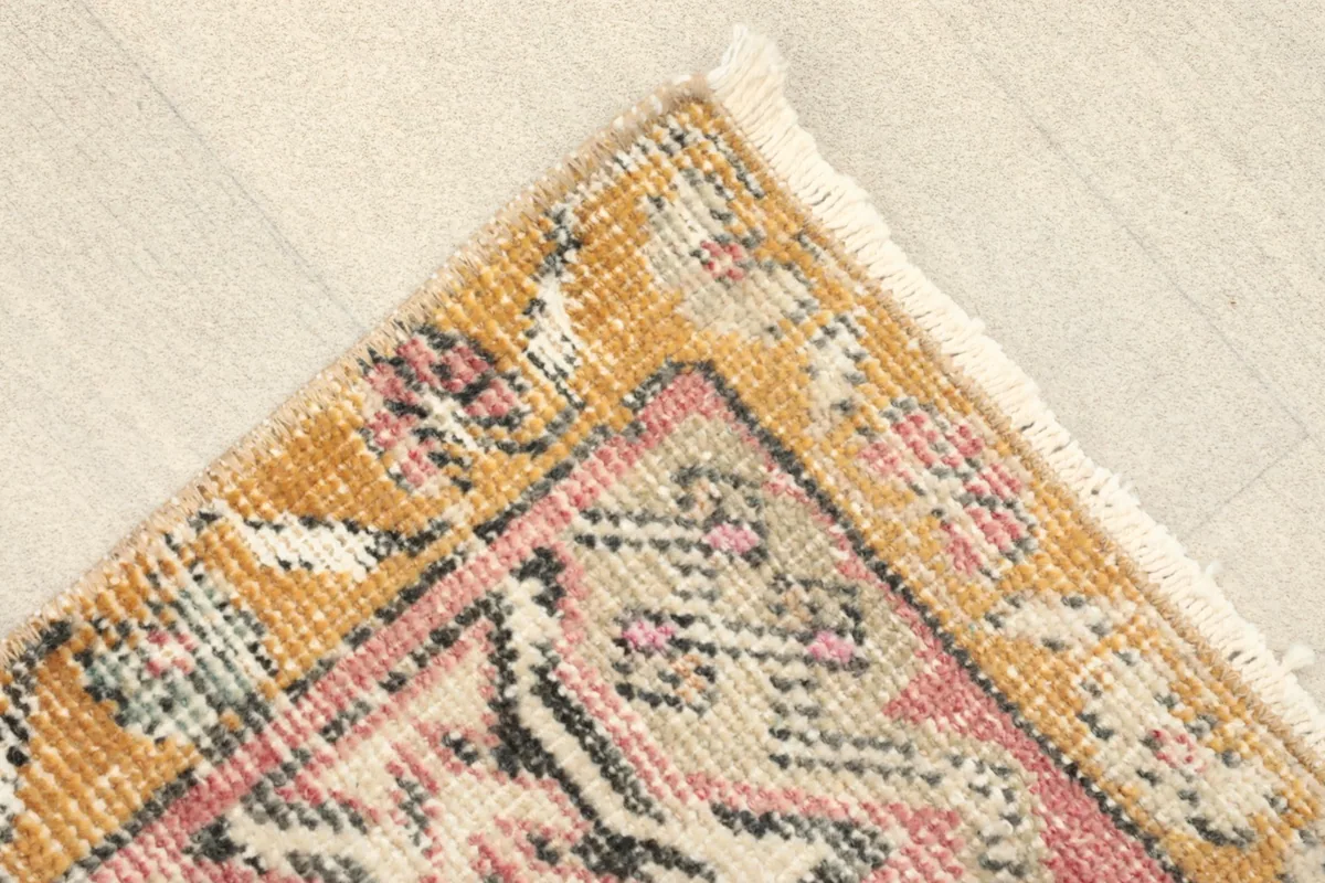Corner detail showing the gold border, rose field, and short fringe of the hand-knotted rug.