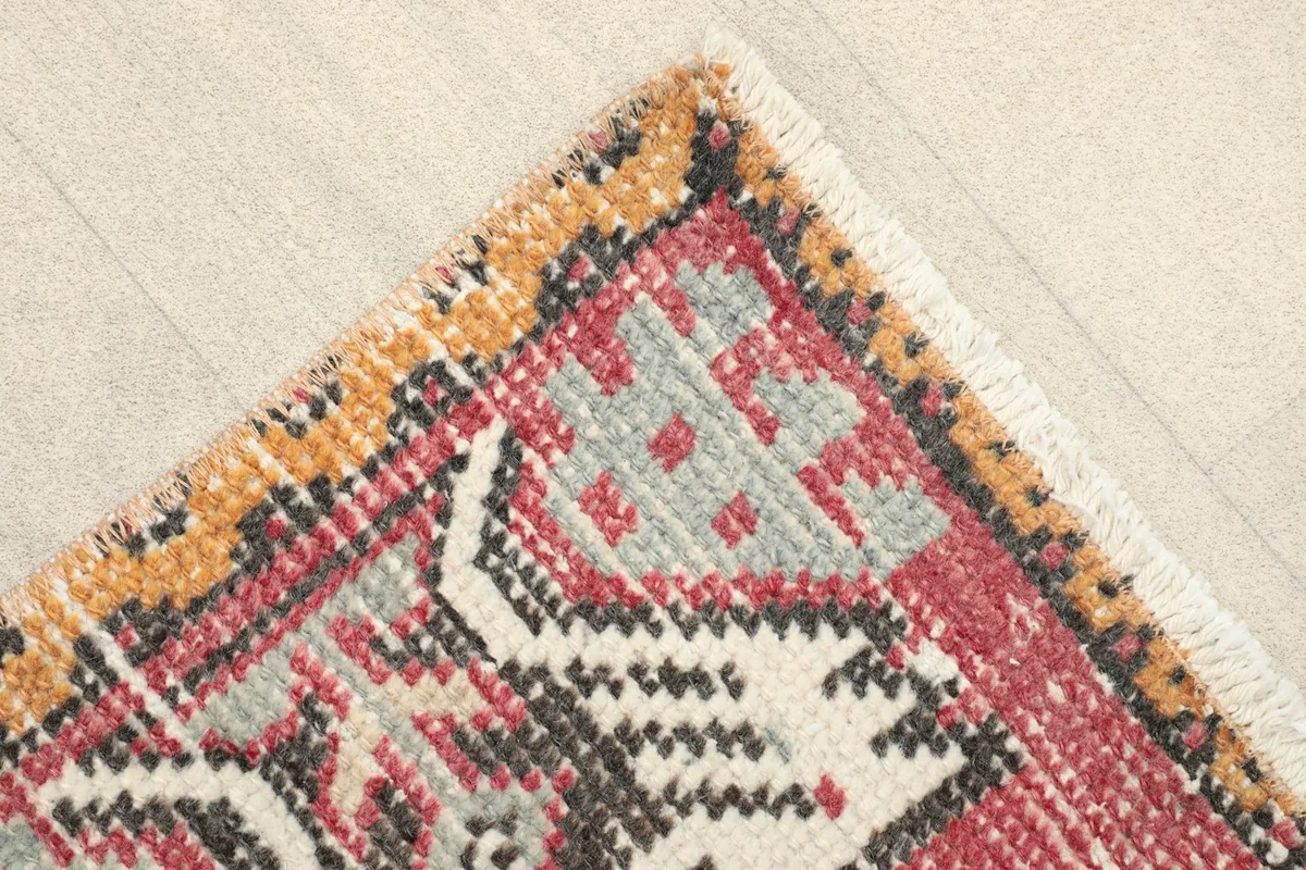 Corner detail showing the outer border in gold and black, with the faded rose field and fringe.