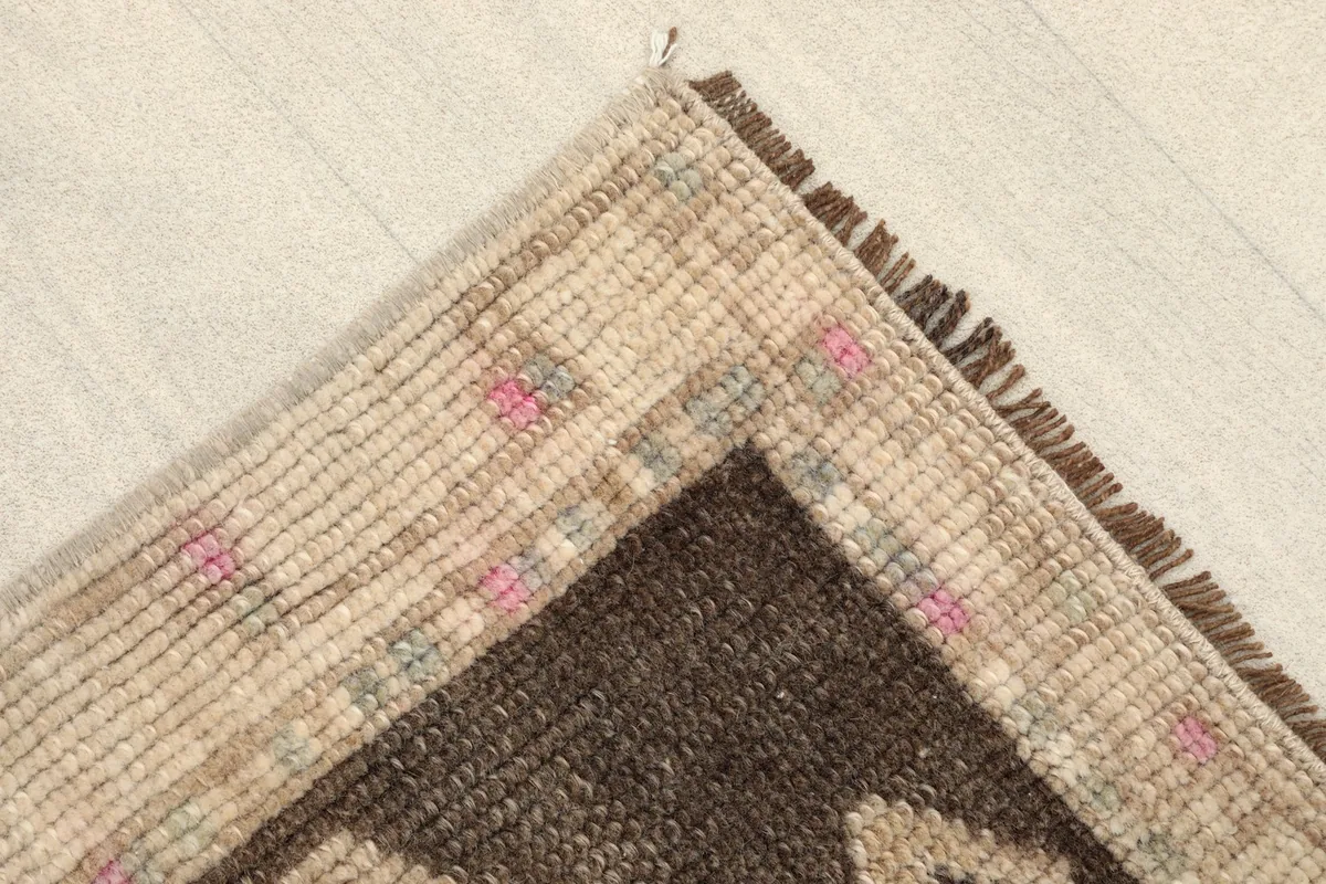 Corner detail showing the beige border and fringe of the vintage doormat.