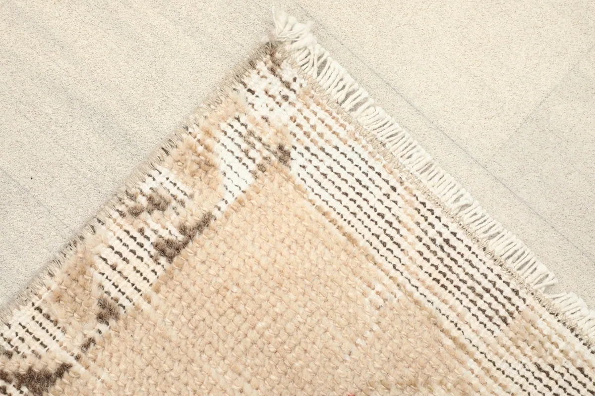 Corner view of the distressed side, showing the lighter beige border and fringe.
