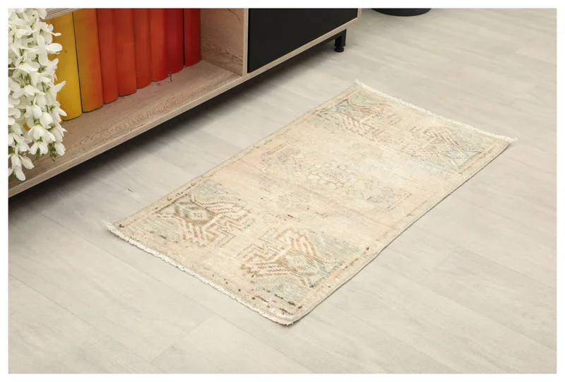Full top view of the beige geometric tribal rug on a light floor next to a low shelf and white flowers.