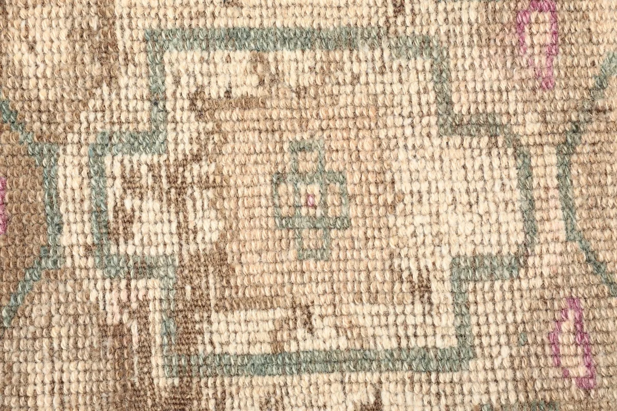 Close-up detail of the beige field and a central geometric motif in green and rose.