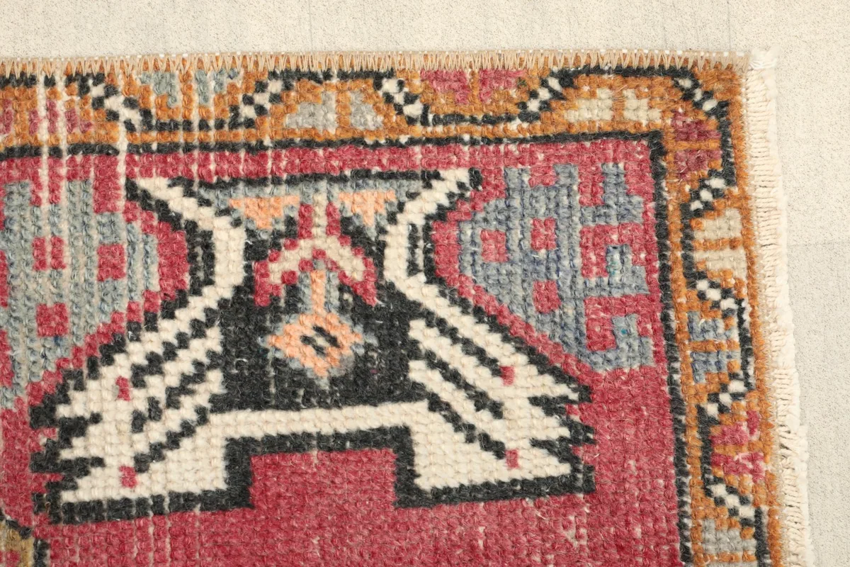 Close-up of a tribal motif in black and ivory on the rose field, showing slight wear.