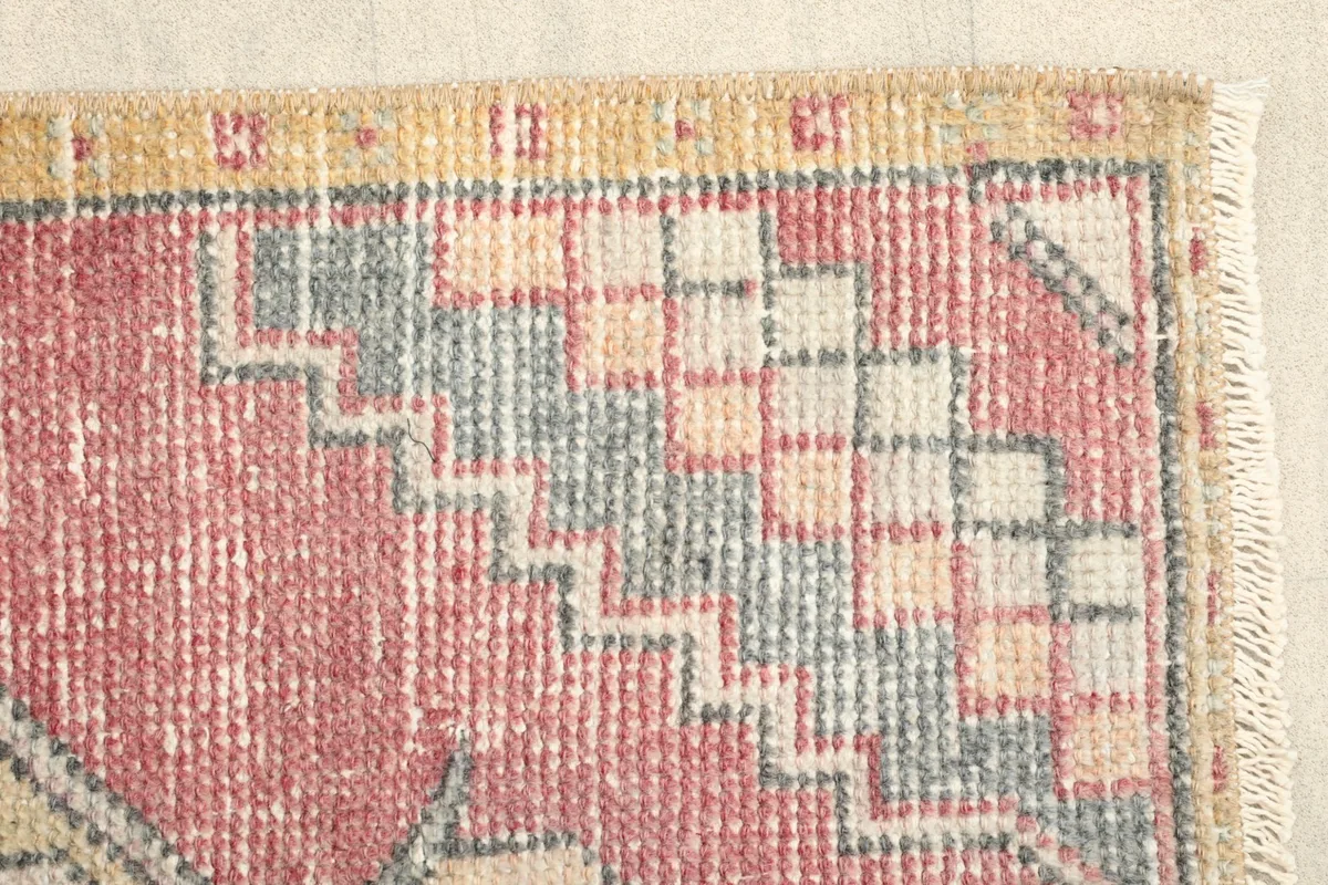 Close-up of the rug's edge, revealing the faded rose color and geometric motifs.
