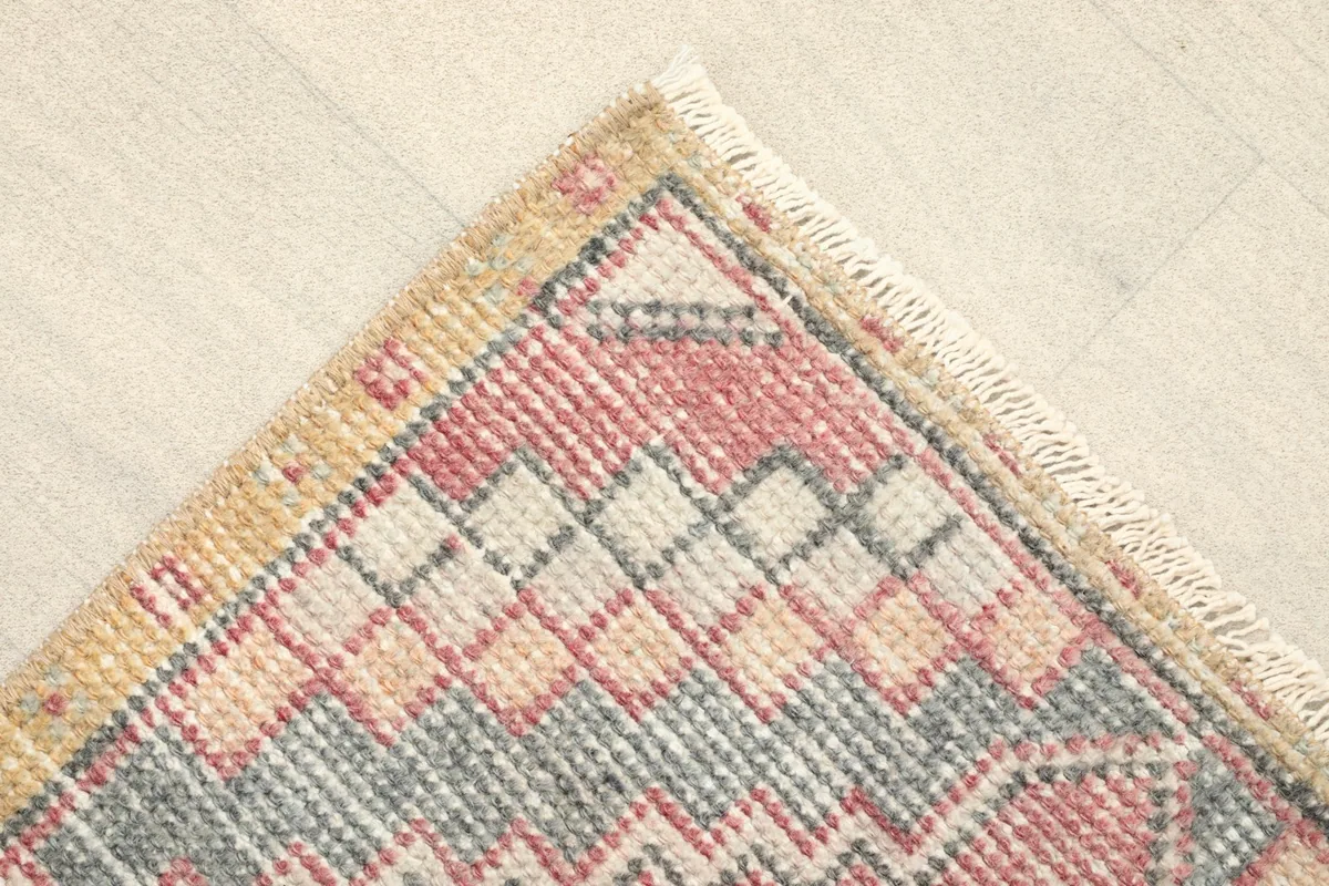 Detail of the corner, showing the gold border and tribal patterns in rose, gray, and beige.