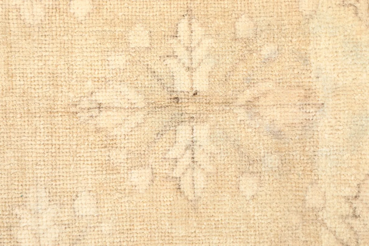 Close-up detail of a central floral motif and the low pile texture of the vintage beige rug.