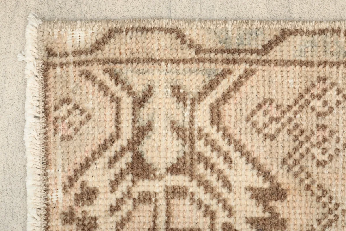 Close-up detail of the rug's corner showing beige pile, brown geometric patterns, and fringe