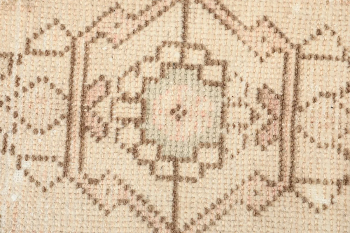 Close-up of the central pattern, showing subtle pink and blue threads within the beige and brown design