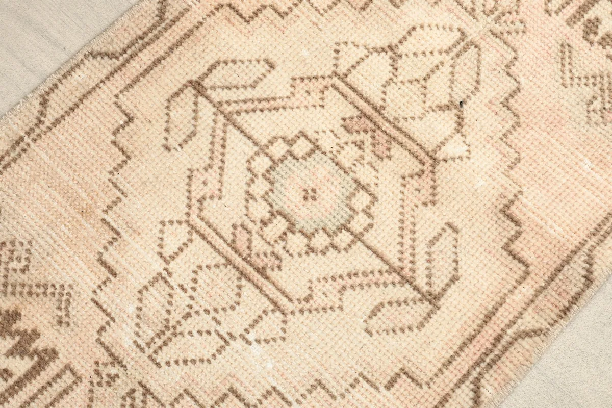 Overhead view of the rug's central medallion-like geometric pattern in brown on a beige field