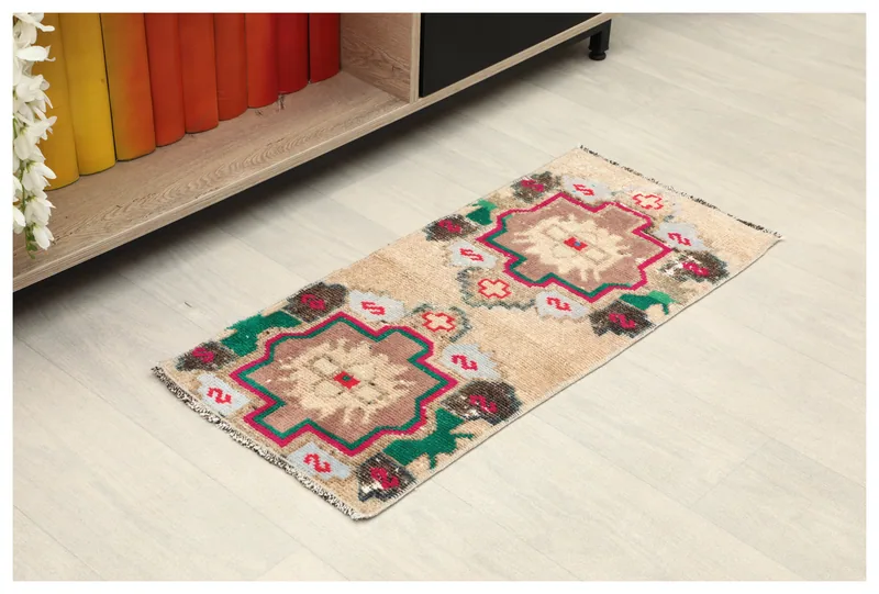 Full top view of the 1'3" x 2'7" beige tribal medallion doormat on a light floor next to a bookshelf.