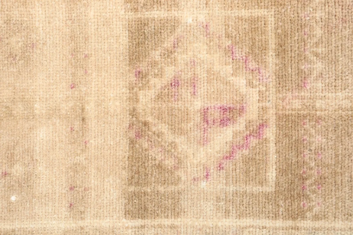 Close-up detail of the central geometric pattern in rose and beige, showing the wool pile texture.