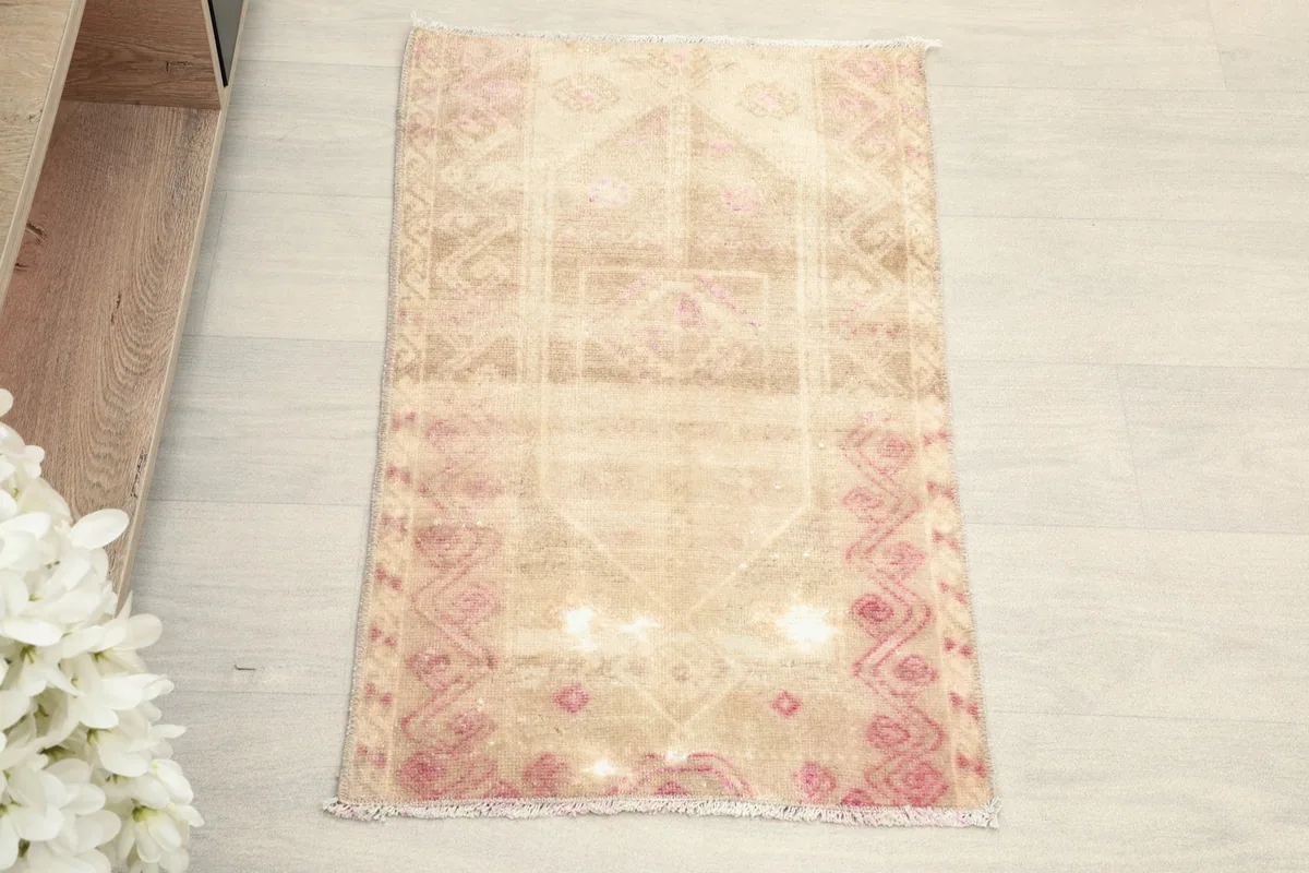 Overhead view of the small beige vintage rug with rose geometric patterns.