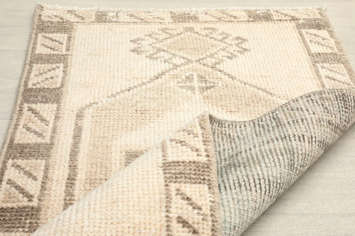 Angled view of the rug with a section folded back, showing the wool pile and cotton foundation.