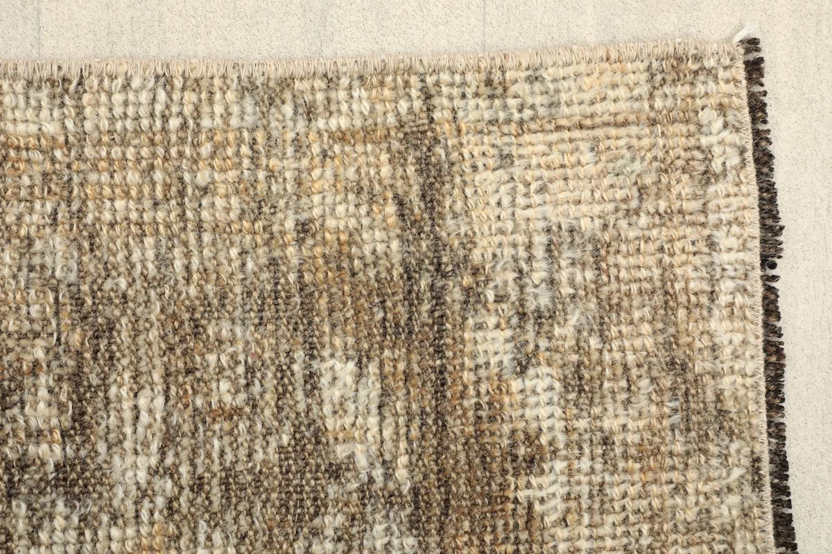 Close-up detail of the low pile texture and distressed areas with beige, brown, and charcoal threads