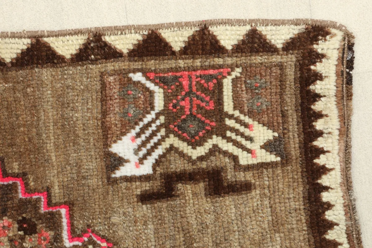 Close-up of a tribal motif near the rug's edge, showing the pink, brown, and ivory colors