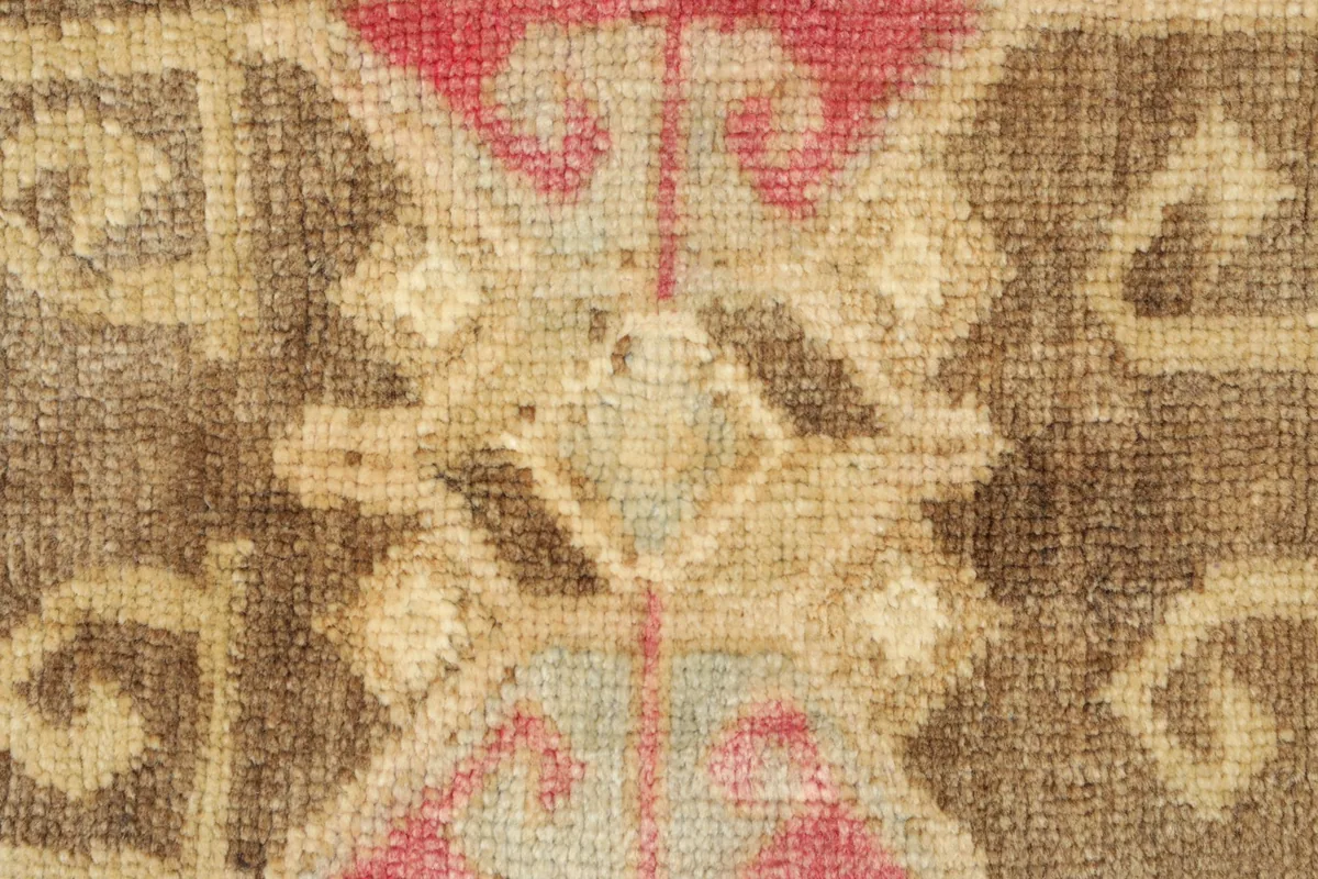 Close-up detail of the rug's central motif, featuring rose, cream, and brown wool pile.